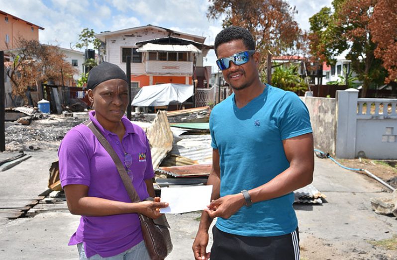 Captain of the Guyana Jaguars, Leon Johnson, hands over the donation on behalf of his team to victim of the Pike Street fire, Angela Dominic. (Samuel Maughn photo)