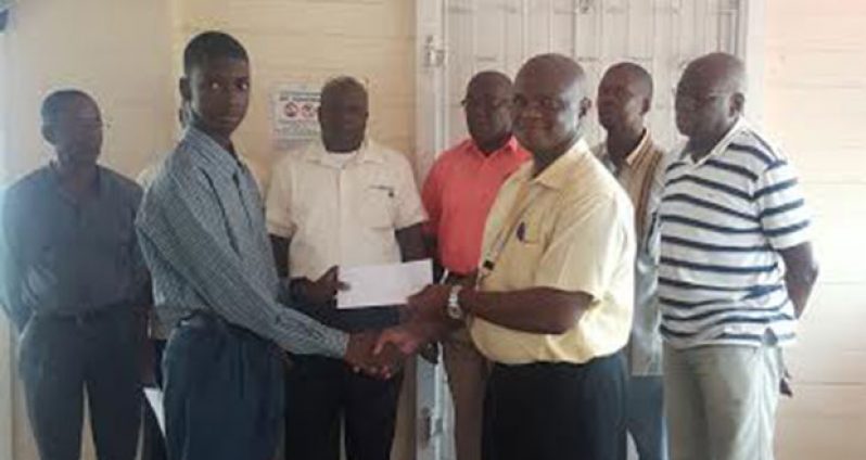 Clyde Layne, Treasurer of GAPSO, hands over a cheque to Jamal Thomas as his father, Milton Thomas, (second from right) and other members of GAPSO look on