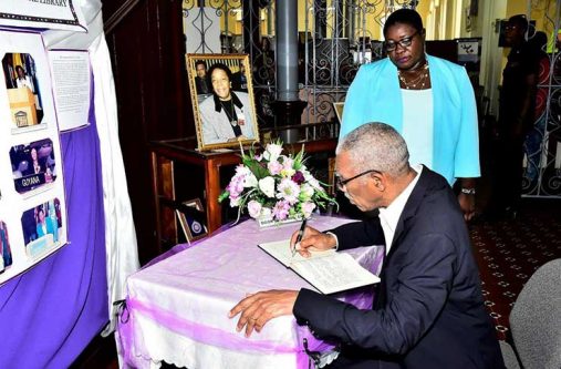 President David Granger signing the book of condolence for the late Ms. Carmen Jarvis at the National Library, while Chief Librarian, Ms. Emily King looks on