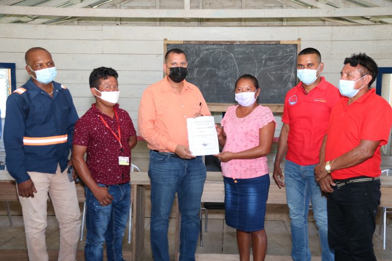 Housing and Water Minister, Collin Croal, hands over the first contract in the community of Jawalla to Toshao, Verron Henry, while flanked by other officials