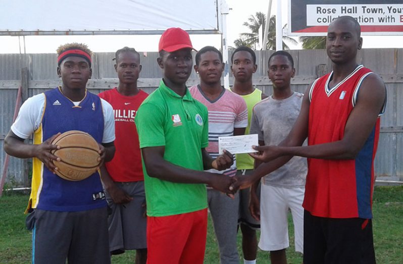 Kevlon Anderson hands over the donation to Perry Cort of the Rose Hall Town  basketball team.
