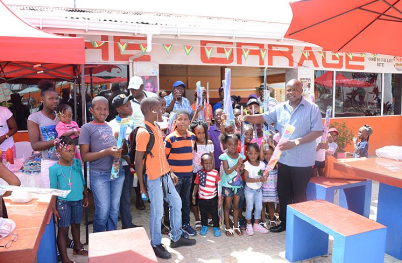 Former Presidential Adviser on Youth Empowerment, Aubrey Norton, hands over some of the kites during the day-long distribution, while the businessmen, at rear, look on. (Rabindra Rooplall photo)