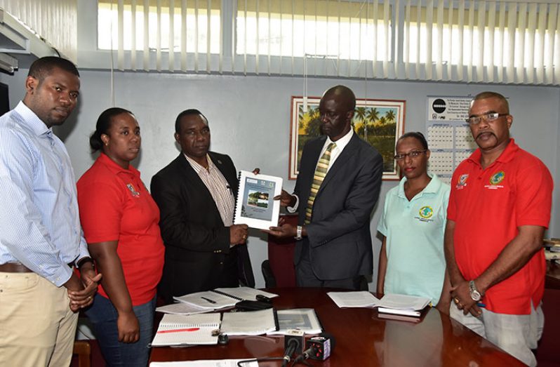 FAO Representative Rueben Robertson presenting a copy of the proposed project document to Guyana Lands and Surveys Commissioner Trevor Benn, in the presence of Manager of the Surveys Division, Rene Duesbury and the Commission’s Legal Advisor, Yolanda Lamott on the right and the Senior Land Administration Officer, Jewel Cheong and Policy Analyst, Durwin Humphrey, on the left.