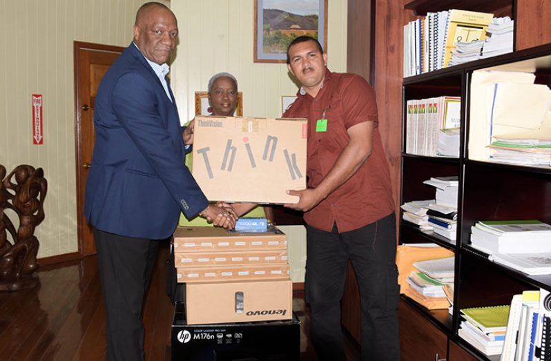 Minister of State, Mr. Joseph Harmon, left, hands over computer supplies to Aranaputa Village Chairman,
Mr. Adon Jacobus, right, with the help of Ms. Roxanne
Barratt, centre