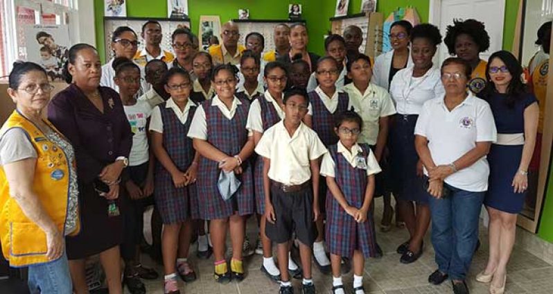 In photo, recipients and their parents, together with Headmistress of the New Diamond-Grove Primary School, Ms. Chichester, pose with management staff of Optique Vision Care and members of the Diamond-Grove Lions Club