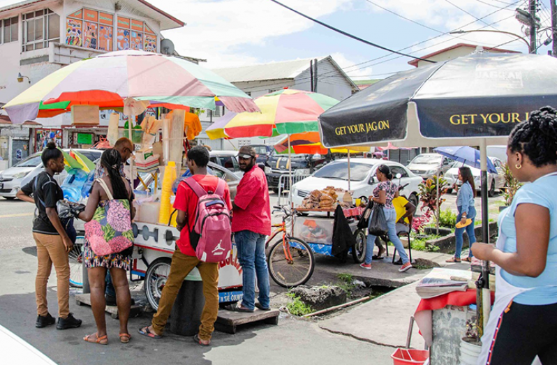 Patrons and a snow-cone vendor, none of whom appear to be wearing face masks, await their turn at a snow-cone cart outside the Bourda Market this week