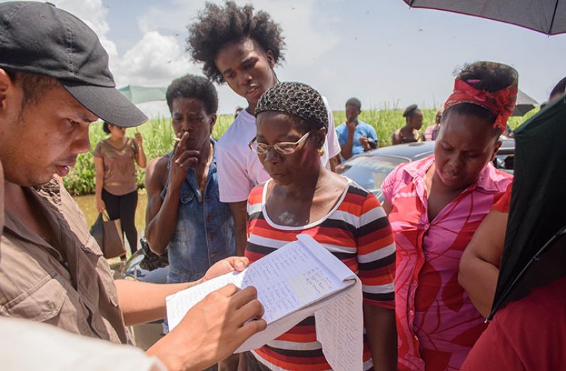 One prison service officer (left) tries to confirm whether this woman’s relative is being housed at the Lusignan Prison
