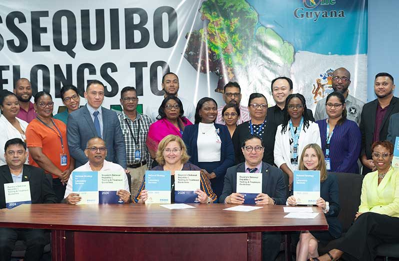 Chief Medical Officer (CMO) of Guyana, Dr. Narine Singh (extreme left, seated), the Minister of Health, Frank Anthony (seated, second from left), the Director of the Department of Global HIV, Hepatitis, and Sexually Transmitted Infections Programmes (HHS) at the World Health Organisation (WHO), Dr. Meg Doherty (sitting right of Dr. Anthony), and the Officer-in-Charge, PAHO/WHO Guyana, Mr. Daniel Albrecht, display their guidelines and laboratory services books along with other officials and staff of the MoH 