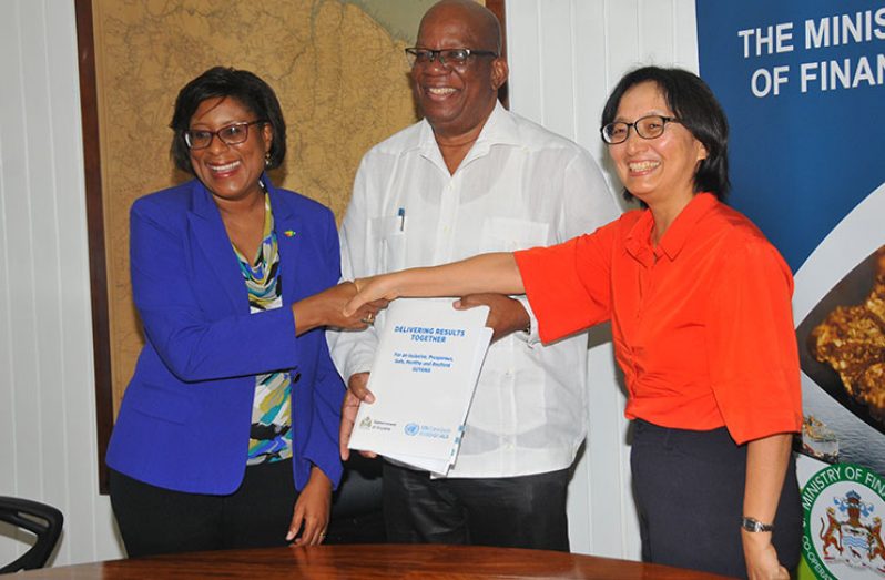 Finance Minister Winston Jordon hold the signed document as Minister Catherine Hughes exchanges a handshake with UNDP Resident Coordinator, Mikiko Tanaka (Adrian Narine photo)