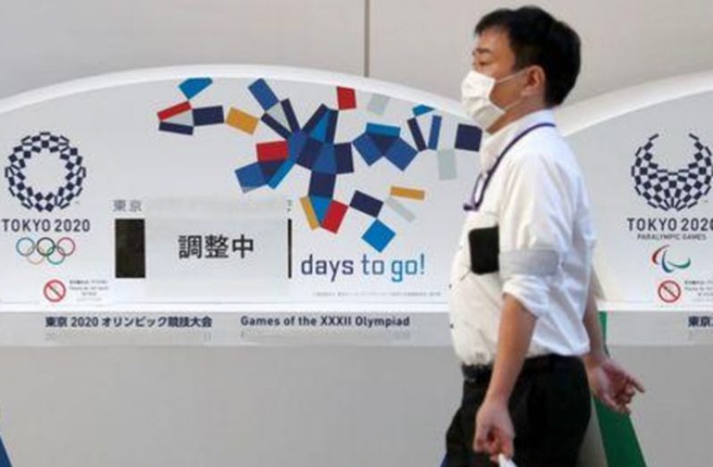 A man wearing a protective face mask due to the outbreak of coronavirus disease (COVID-19) walks past countdown clocks for the opening of Tokyo 2020 Olympic and Paralympic Games that are currently covered with banners that read 'Adjusting', in Tokyo, Japan, yesterday. (REUTERS/Issei Kato)