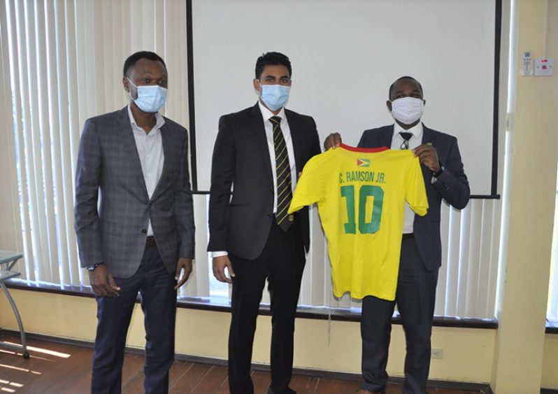 GFF president Wayne Forde (right) presents a customised ‘Golden Jaguars’ replica jersey to Minister Ramson in the presence of Dion Inniss.
