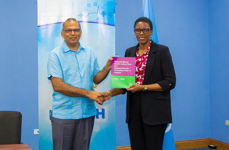 PAHO/WHO Assistant Director Dr. Rhonda Sealey-Thomas (right) hands over the National Mental Health Action Plan and National Suicide Prevention Plan for Guyana 2024-2030 to Minister of Health Dr. Frank Anthony