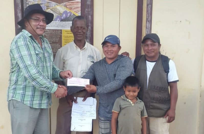 Adviser to the Minister of Indigenous Peoples’ Affairs, Mervyn Williams (left) handing over the cheque at Kumu Villiage in Region 9