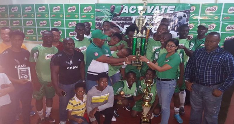 Chase Academy Principal Henry Chase accepts the winning trophy from Milo Brand representative Renita Sital in the presence of players and other officials.