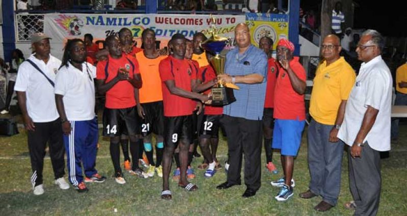 Minister Juan Edghill hands over the winning trophy and cheque to Alpha United captain Dwight Peters in the presence of his fellow teammates and technical staff.