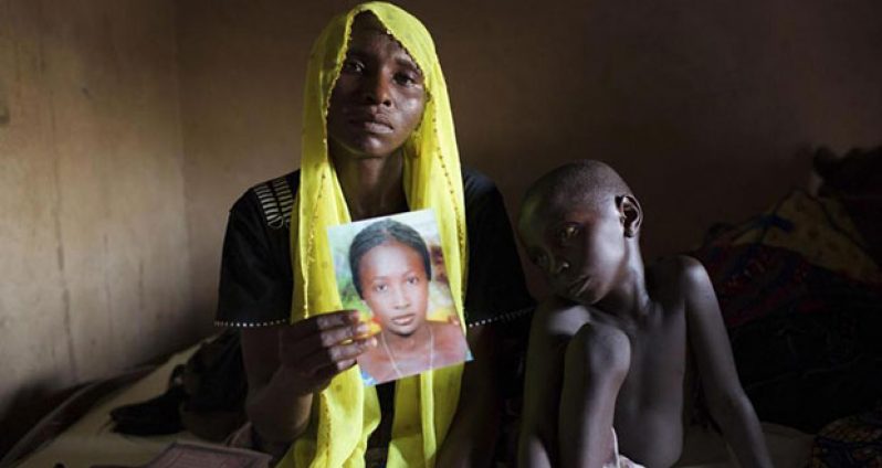 Rachel Daniel, 35, holds up a picture of her abducted daughter Rose Daniel, 17, as her son Bukar, 7, sits beside her at her home in Maiduguri in this May 21, 2014 file photo. REUTERS/Joe Penney/Files