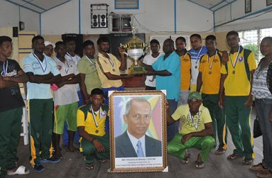 Former MP and General Secretary of PNC/R Aubrey Norton (right) presents the trophy to captain of the victorious Regal XI team Mohamed Ayube, in the presence of other members, who strikes a pose with a portrait of the late Winston Murray.