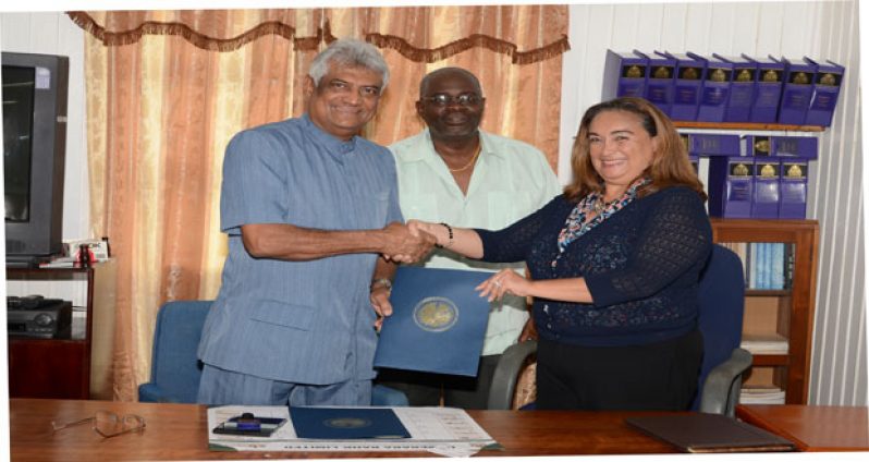 GECOM Chairman Dr Steve Surujbally and former Foreign Minister of Belize, Ms Lisa Shoman, Head of the OAS Election Observer Mission, exchange copies of an agreement they signed yesterday. Standing, at centre in photo, is Chief Elections Officer Mr Keith Lowenfield