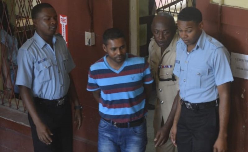 Assistant Superintendent , Seecharran Singh ( in stripe top) being led to the courtroom by police ranks on Thursday.