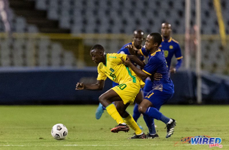 Guyana’s Omari Glasgow (left) tries to hold off a Barbados opponent during international action at the Hasely Crawford Stadium on 27 March 2022. (Copyright: Daniel Prentice/ Wired868)