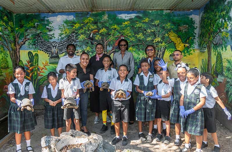 PAC Commissioner, Jason Fraser, Vice President of SLB, Sharlene Seegoolam and THAG’s President Dee George, flanked by students of Mae’s School holding the turtles (Delano Williams photo)