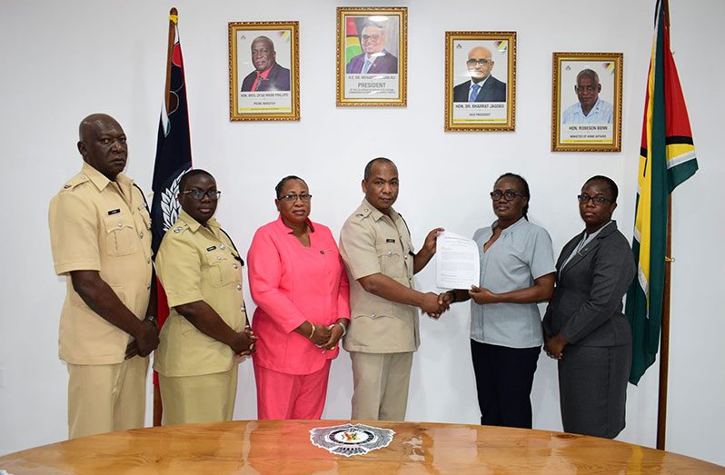 Deputy Commissioner (ag), Calvin Brutus and Officer in Charge of Admin/Human Resource, Dianne Wong, exchanged a signed copy of the MoA.  Others present include: from left, Force Training Officer, Superintendent Keithon King; Head of the Force's Strategic Planning Unit, Woman/Assistant Superintendent, Nicola Kendall; Head of the Community Relations Department, Superintendent Crystal Robinson and IPED’s Company Secretary, Juanita Critchlow