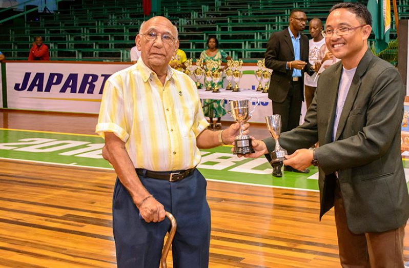 Veteran sport personality Pat Holder handing over the trophies to Suriname’s Director of Sport