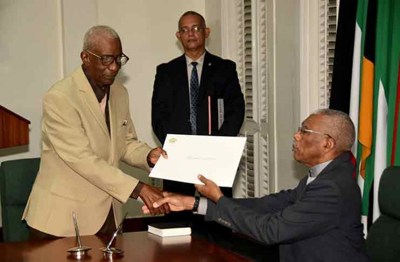 Retired Justice James Patterson receives his instrument of appointment from President David Granger at his swearing-in as chairman of the Guyana Elections Commission