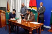 Newly-sworn in Commissioner Ms. Pauline Chase signs the official appointment document alongside President Dr. Irfaan Ali