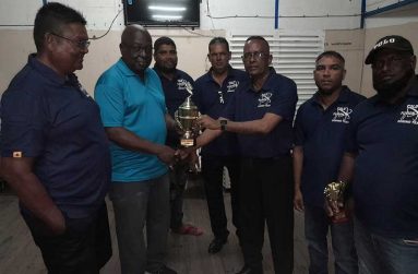 Regal Sports Manager Ian John hands over the winning trophy to Cold Fusion’s skipper Boodnarine Persaud in the presence of his other players.