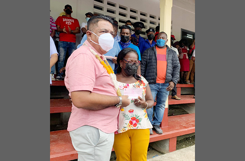 Agriculture Minister, Zulfikar Mustapha, hands over the cheque to one of the beneficiaries, Ava Smith, at Skeldon Community Centre Ground