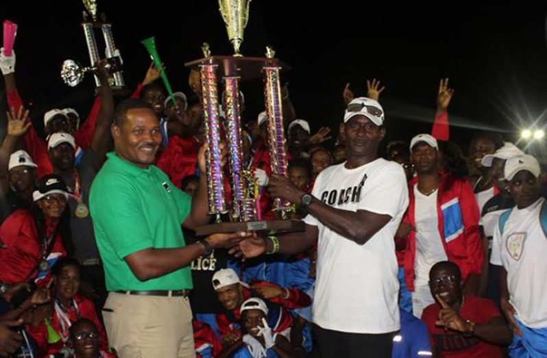 Head coach of the Police team Lyndon Wilson (right) collects the championships trophy in the presence of his elated athletes. (GPF photo)