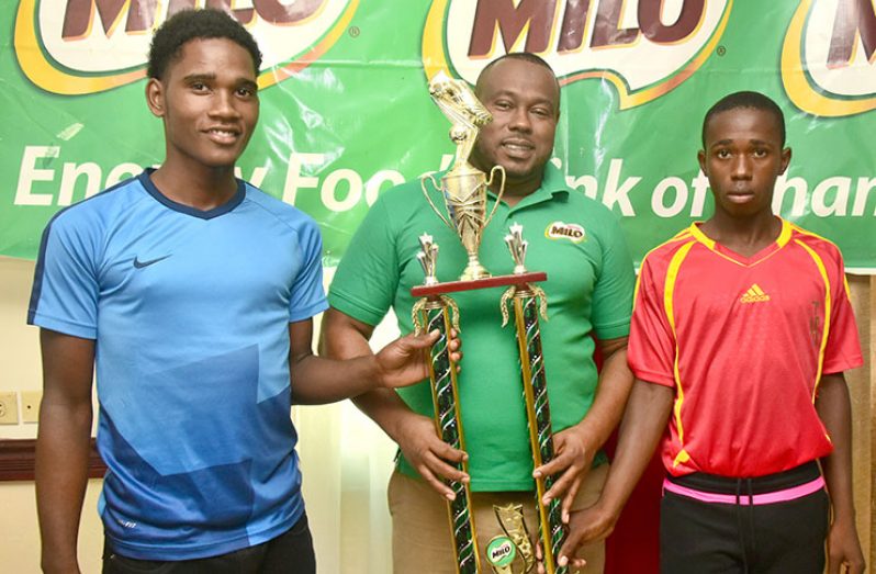 Petra co-Director Troy Mendonca stands with the two finalists for the 2018 Milo schools football tournament. (Adrian Narine photo)