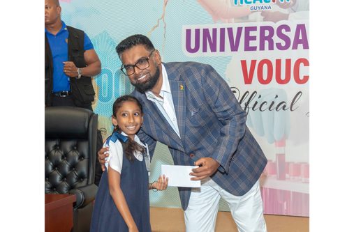 President, Dr. Irfaan Ali presents one of the universal healthcare vouchers to a school child (Yohan Savory photos)