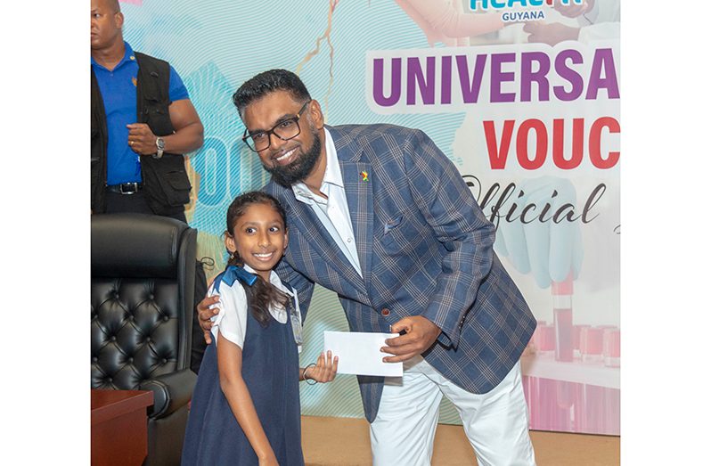 President, Dr. Irfaan Ali presents one of the universal healthcare vouchers to a school child (Yohan Savory photos)