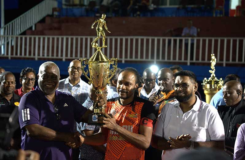 President Dr. Irfaan Ali (right) and Prime Minister Mark Phillips hand over the trophy to Slingerz FC’s Quincy Adams (PHOTO: Slingerz FC)