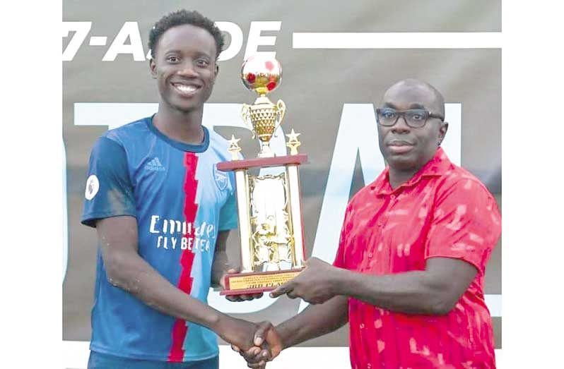 Minister within the Office of the Prime Minister Kwame McCoy presents the captain of the winning team his prize.