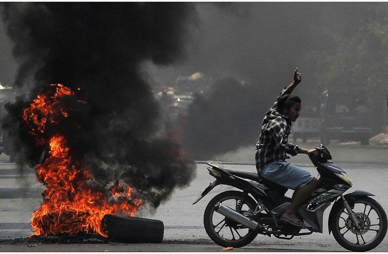 Man flashes the three-finger salute as he passes burning tyres during a protest against the military coup, in Mandalay, Myanmar (Photo courtesy of Reuters/Stringer)
