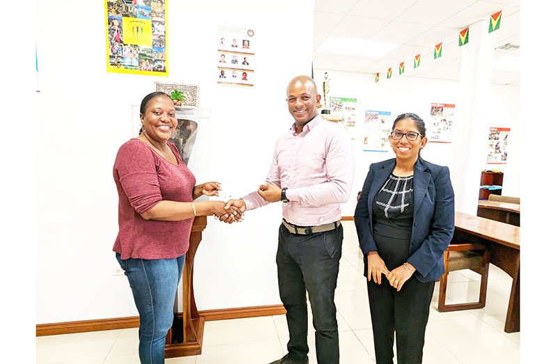 From left, Secretary of the GRFU, Petal Adams receives the cheque from Godfrey Munroe in the presence of GOA Secretary-General, Vidushi Persaud-McKinnon