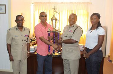 Proprietor of Trophy Stall, Ramesh Sunich, hands one of the trophies to Deputy Commissioner Paul Williams in the presence of Assistant Commissioner Clifton Hicken.