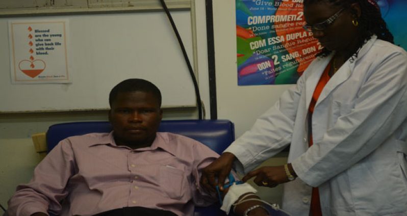 Rawle Nelson donating blood while Keren Jolly demonstrates how the process is done