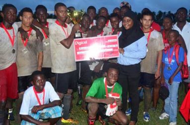 Digicel’s Quality Assurance Agent/Trainer Jamel Denny makes the presentation of the $100 000 cheque to captain of the victorious Bush Lot Secondary School team Marlon Nicholson, while his teammates and supporters look on appreciatively. Stooping at front in green jersey with goalkeeping gloves is Osbert Cain. (Photo by Adrian Narine)