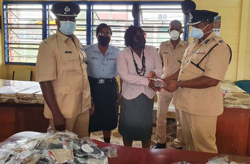 Regional Executive Officer (REO) of Region Three, Jennifer Ferreira- Dougall, handing over face masks to the Regional Commander, Simon McBean, in the presence of Regional Deputy Commander, Dion Moore, and other ranks of the Guyana Police Force