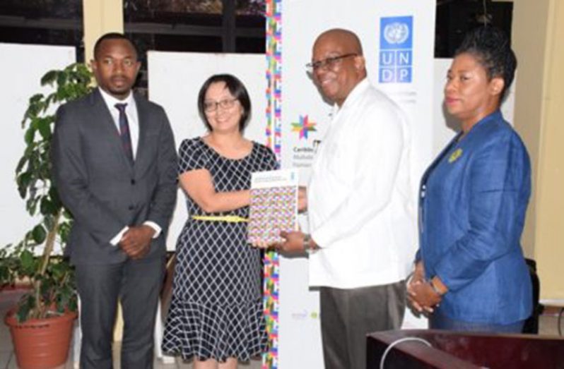 Minister of Finance Winston Jordan receives the CHD Report from UN Resident Coordinator Mikiko Tanaka, while UNDP Regional Advisor Kenroy and Deputy Vice-Chancellor of the UG, Dr Barbara Reynolds, look on
