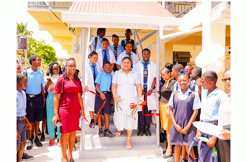 Minister of Education, Priya Manickchand, while being flanked by students, cuts the ceremonial ribbon to the two-storey building that can accommodate approximately 100 students