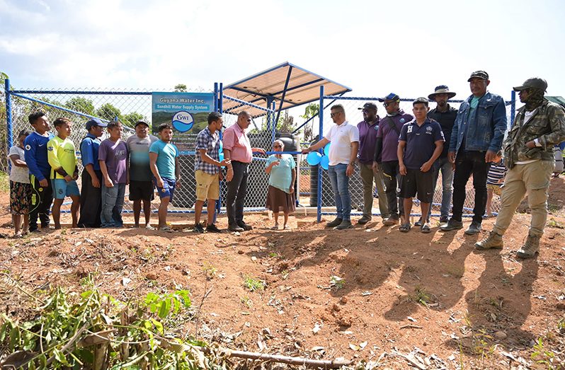 A senior citizen of North Pakaraimas, Region Eight, cuts the ribbon held by Minister of Housing and Water, Collin Croal to commission the $36M water supply system