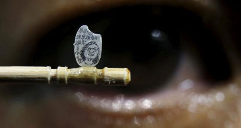 Miniature artist Chen Forng-Shean poses with his latest work, a miniature portrait of Taiwanese president-elect Tsai Ing-wen on a grain of rice, in Taipei, Taiwan April 18, 2016. The Chinese characters read, "Modest, modest and even more modest." (REUTERS/Tyrone Siu)