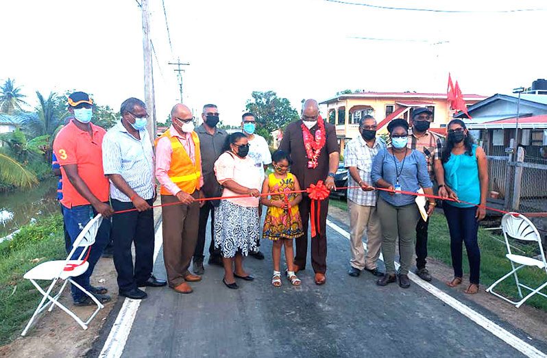 Minister of Public Works, Juan Edghill, residents and representatives of the Vereeniging / Unity NDC, assist a young resident to cut the ribbon to officially commission the rehabilitated roads (Ministry of Public Works photo)