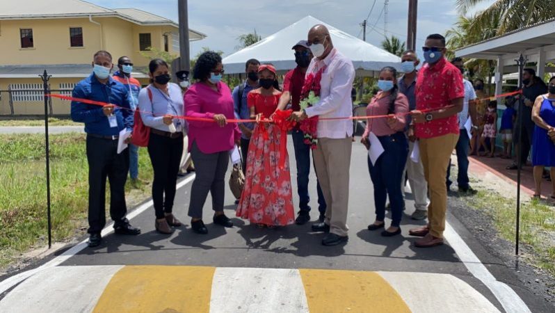 Public Works Minister, Bishop Juan Edghill assisting a young resident to cut the ceremonial ribbon for the opening of one of the new roads in Region Two
