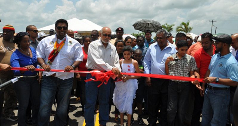 President Donald Ramotar assists the granddaughter of rice farmer and businessman, Bhagwandin Madoo, who provided some of the land for the construction of the access road free to the Government, to cut the ribbon to officially open La Parfaite Harmonie access road